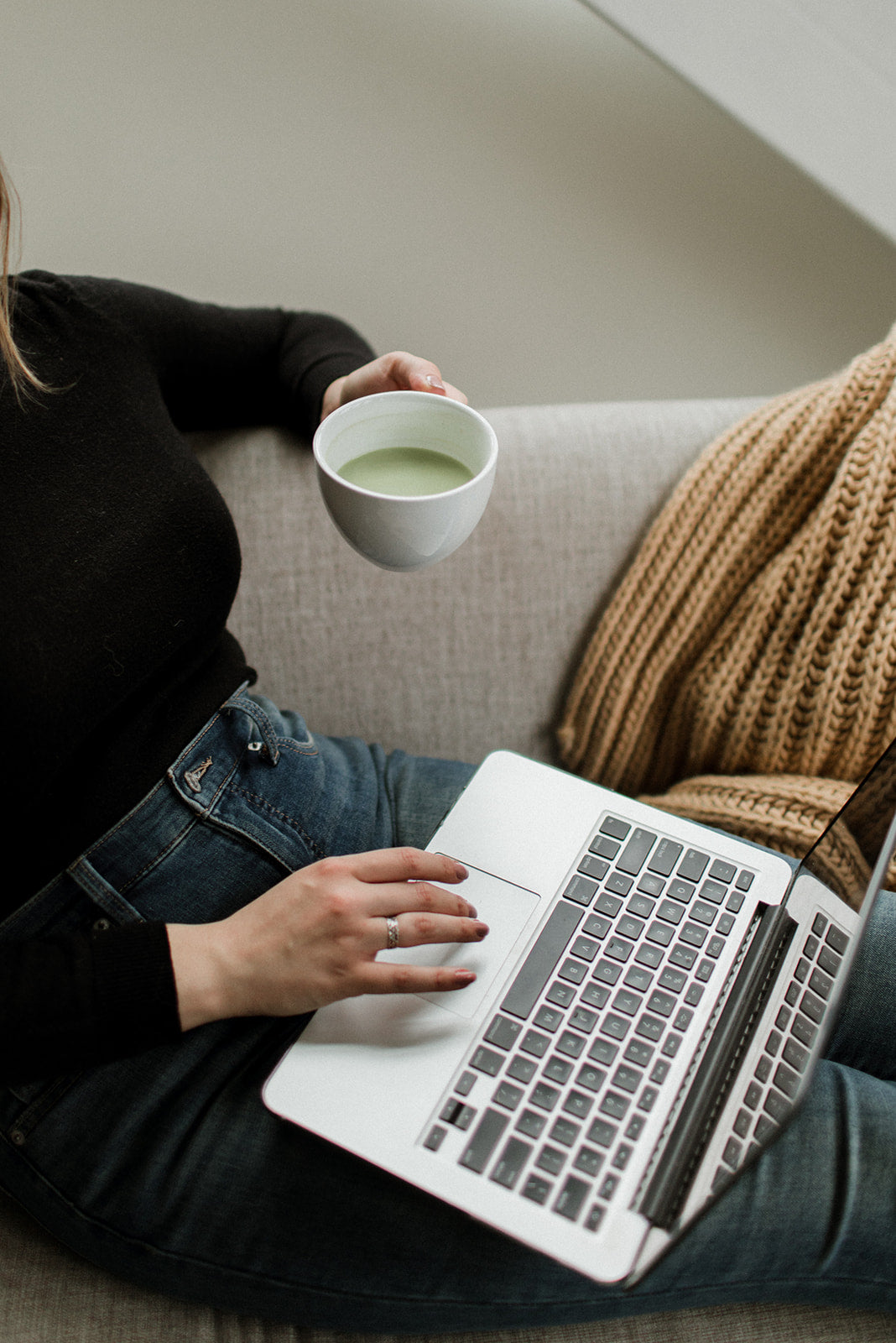 person on couch using laptop with beverage in hand